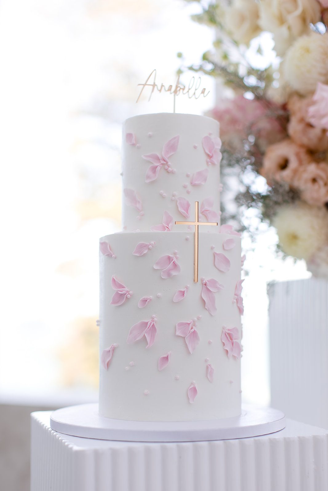Two-tier christening cake with pink petals and a gold cross